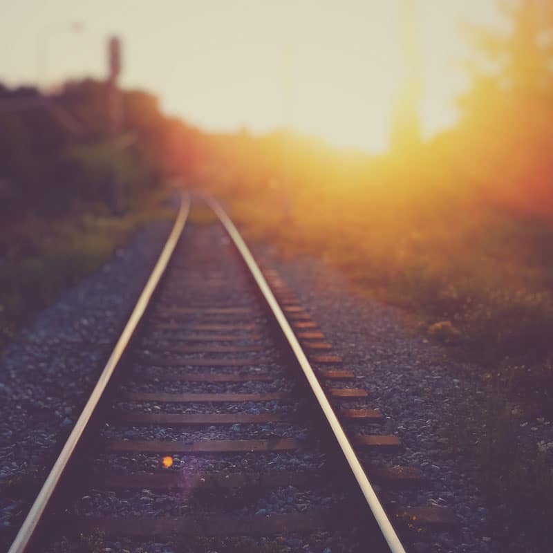 Vue d'une rail de chemin de fer menant vers un soleil couchant.