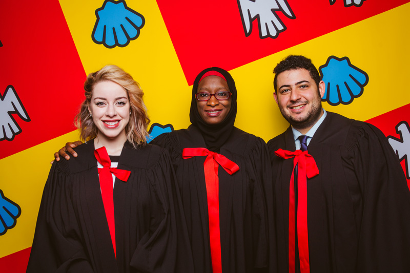 3 diplômés en toges souriant sur fond du drapeau de l'Université Laval