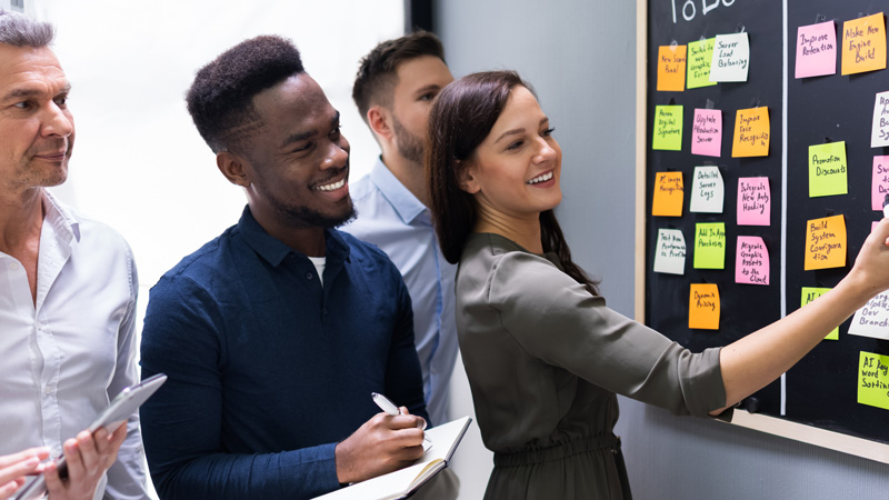 Personnes regardant un tableau noir avec des post-it dessus